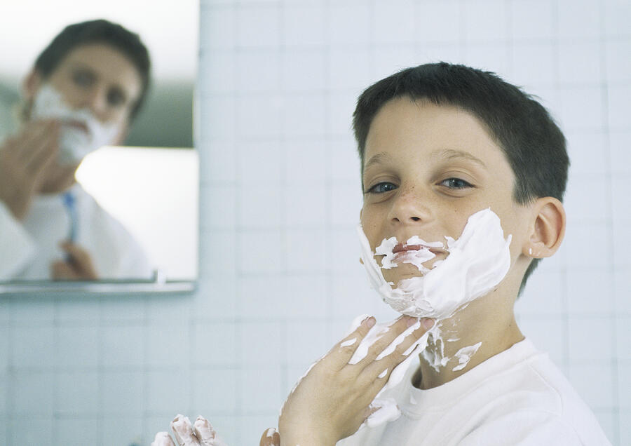 Boy with shaving cream on face and hands, man shaving in background Photograph by Sigrid Olsson