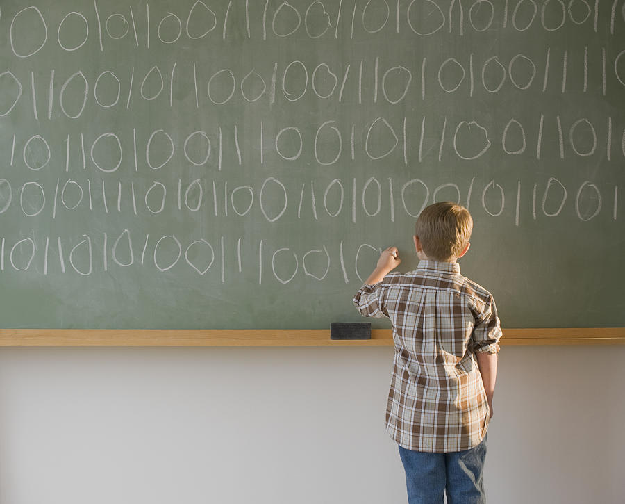 Boy writing binary code on blackboard Photograph by Tetra Images