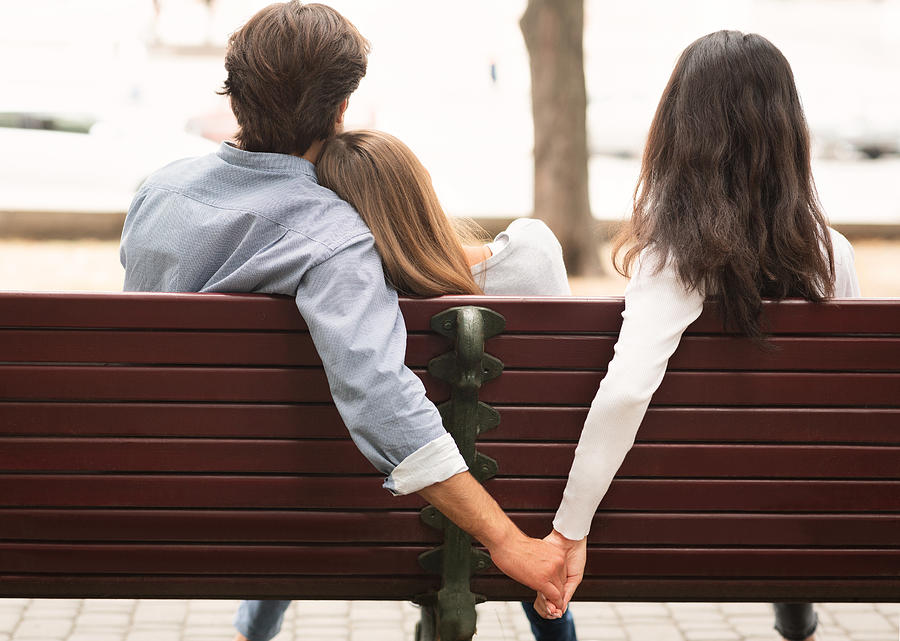 Boyfriend Holding Hands With Girlfriends Friend Sitting On Bench Outdoor Photograph by Prostock-Studio
