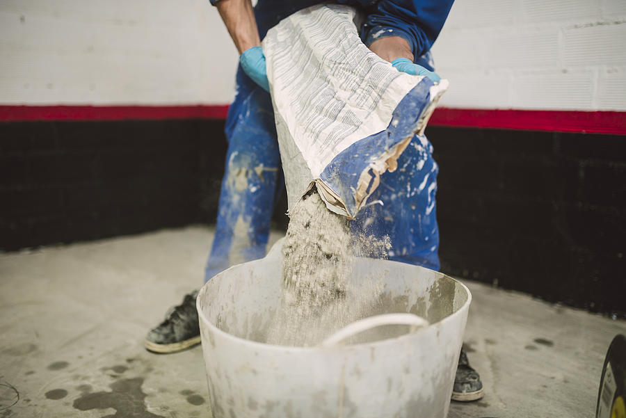 Bricklayer pouring cement powder in bucket Photograph by Westend61