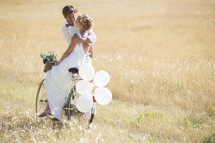 Bride and bridegroom riding bike with balloons attached Photograph by Caiaimage/Tom Merton