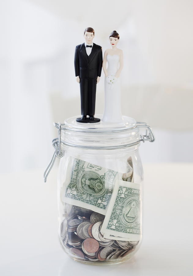 Bride and groom cake toppers on jar of money Photograph by Jamie Grill