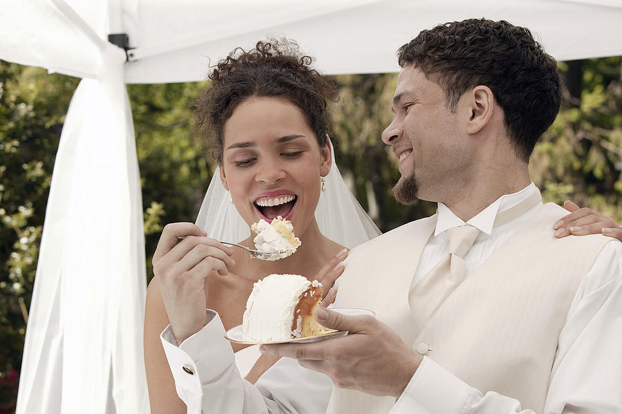 Bride and groom eating wedding cake Photograph by Comstock Images