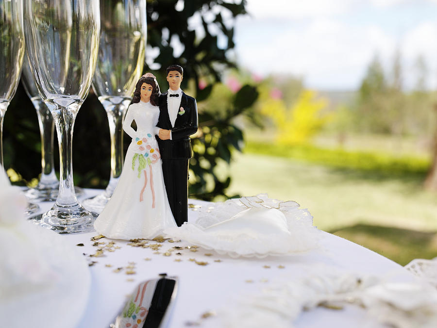 Bride and groom figurine on table by champagne flutes Photograph by Marc Debnam