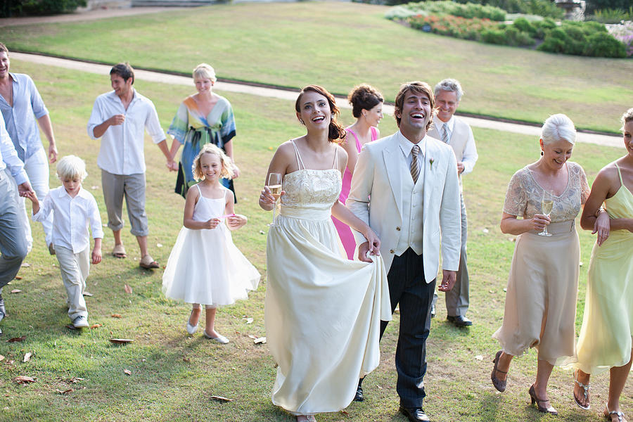Bride, groom and guests walking across lawn Photograph by Tom Merton