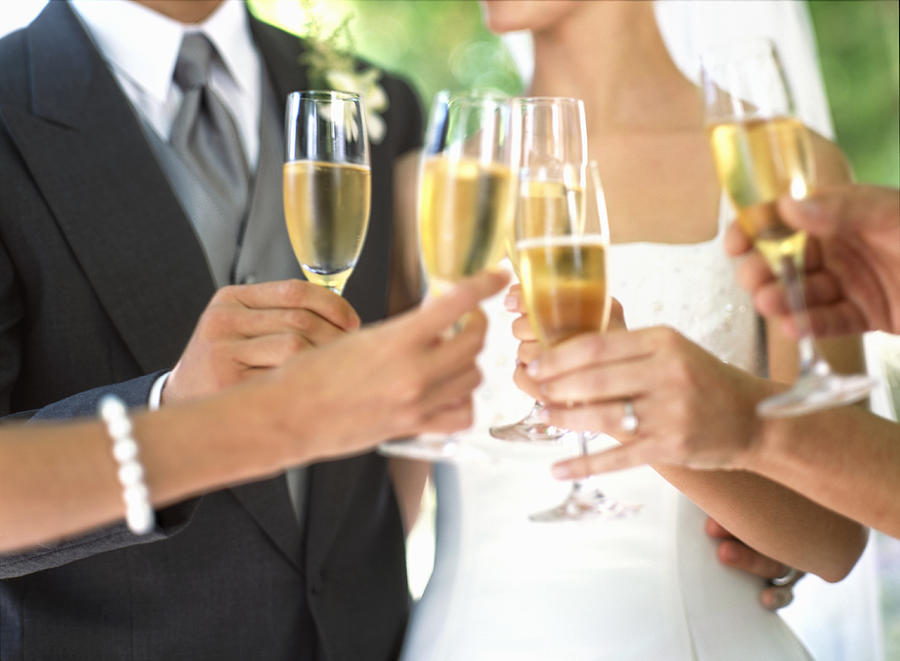 Bride, groom and wedding guests toasting with champagne, mid section Photograph by Todd Pearson