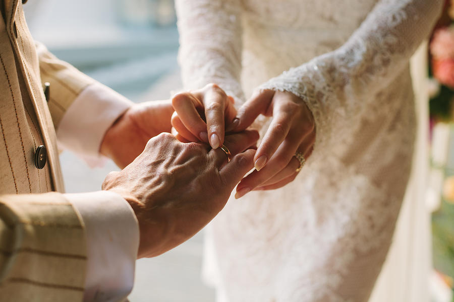 Bride putting ring on grooms finger. Rings exchange. Happy couple celebrating wedding outdoors in summer. Photograph by Anna Blazhuk