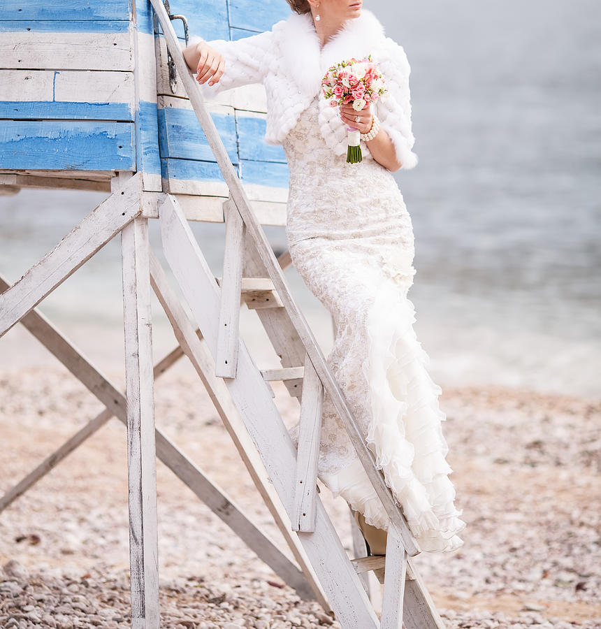 Bride with bouquet by  shore posing on a ladder. Photograph by Manifeesto