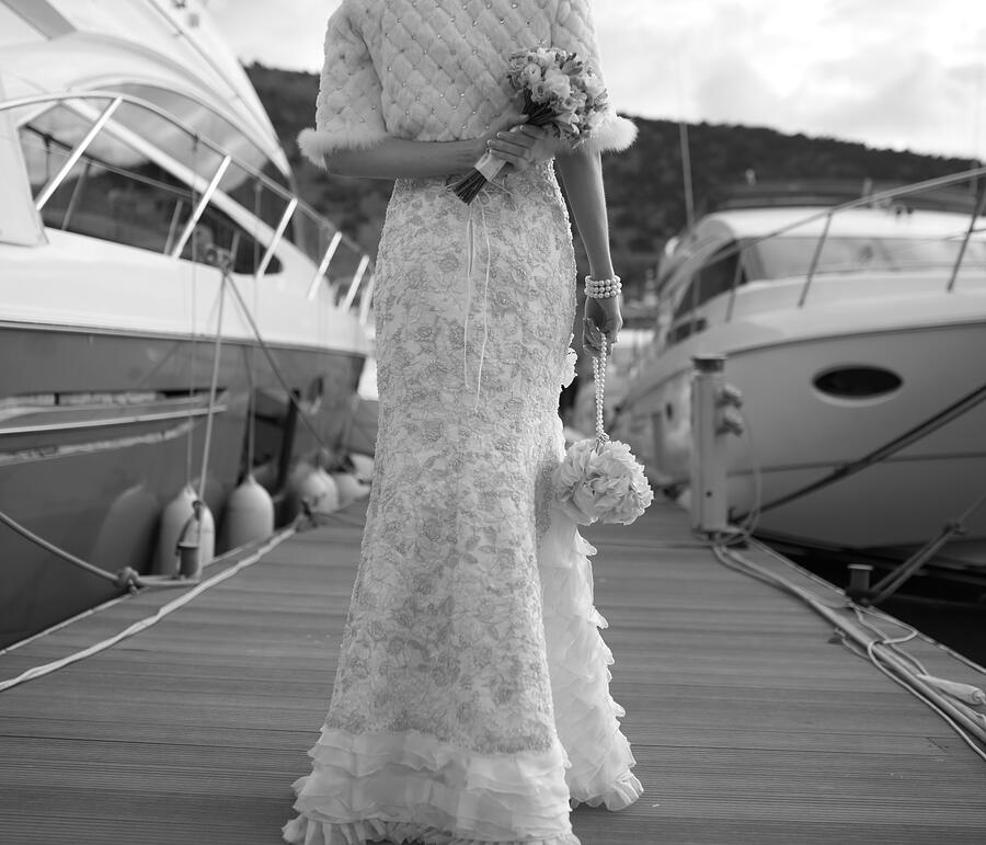 Bride with bouquet walking on pier near  yacht. Photograph by Manifeesto