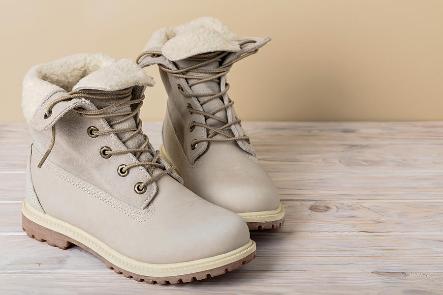 Bright leather winter boots on a light wooden background. Photograph by Oleh_photographer