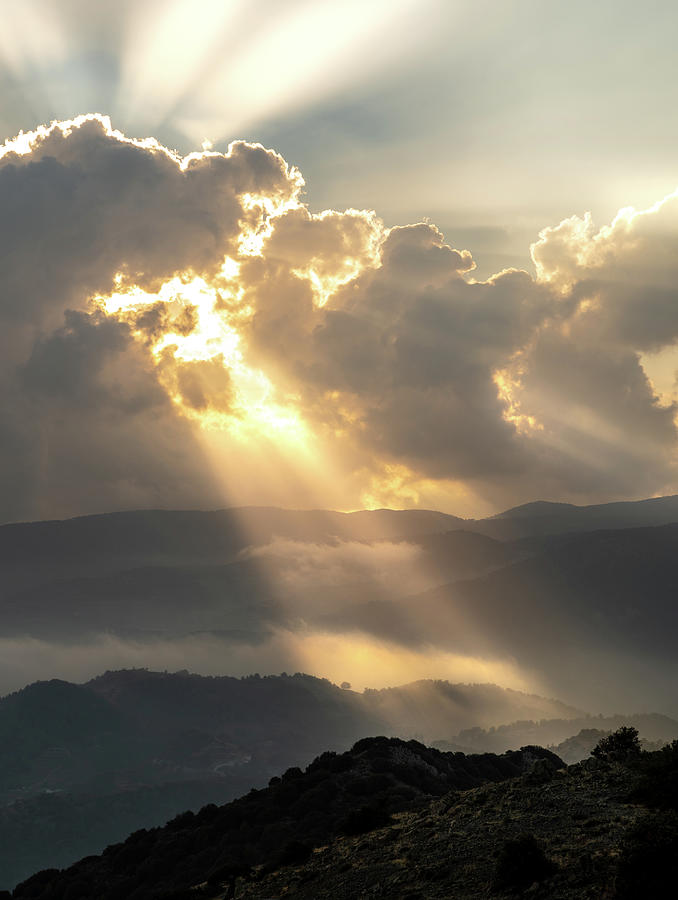 Bright sun rays light shining through dark clouds over mountain at sunset. Dramatic sky in winter Photograph by Michalakis Ppalis