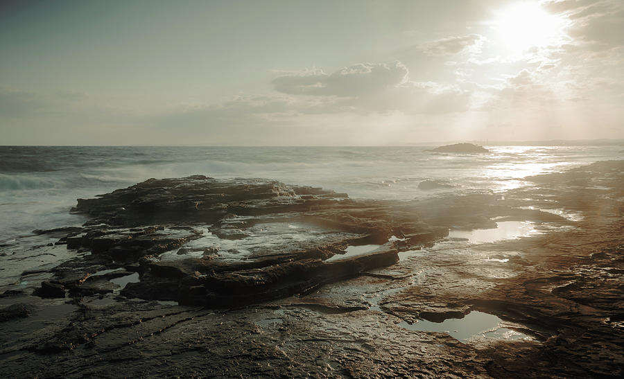 Bright sunlight on a rocky coastline at sunset on a beach. Photograph by Michalakis Ppalis