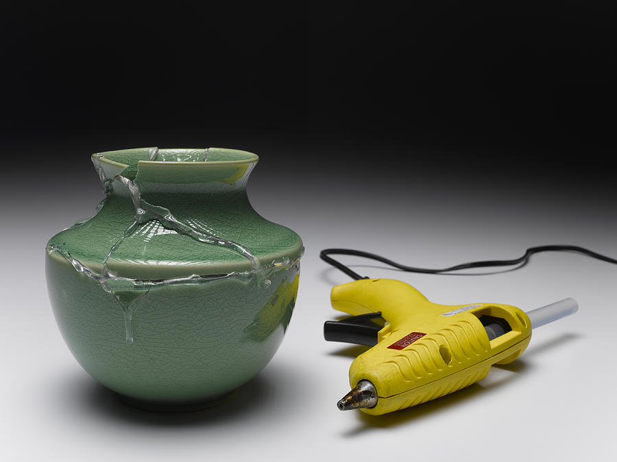 Broken green vase glued together beside yellow glue gun Photograph by Jeffrey Hamilton