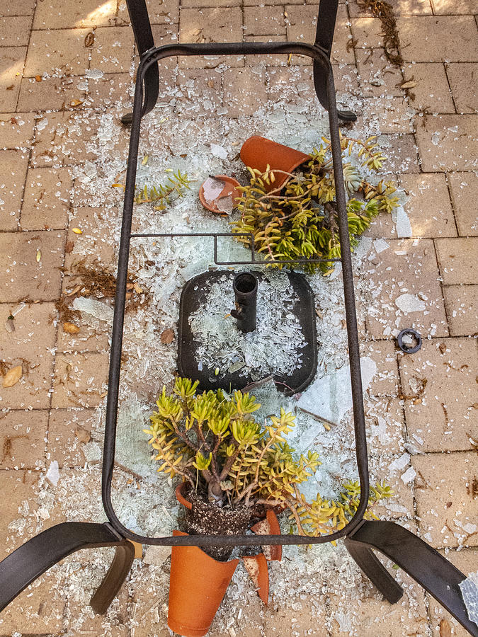 Broken tempered glass patio table upside down with damaged potted plants after a wind storm Photograph by Bill Boch