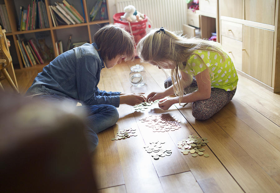 Brother and sister counting coins from savings jar Photograph by Frank van Delft