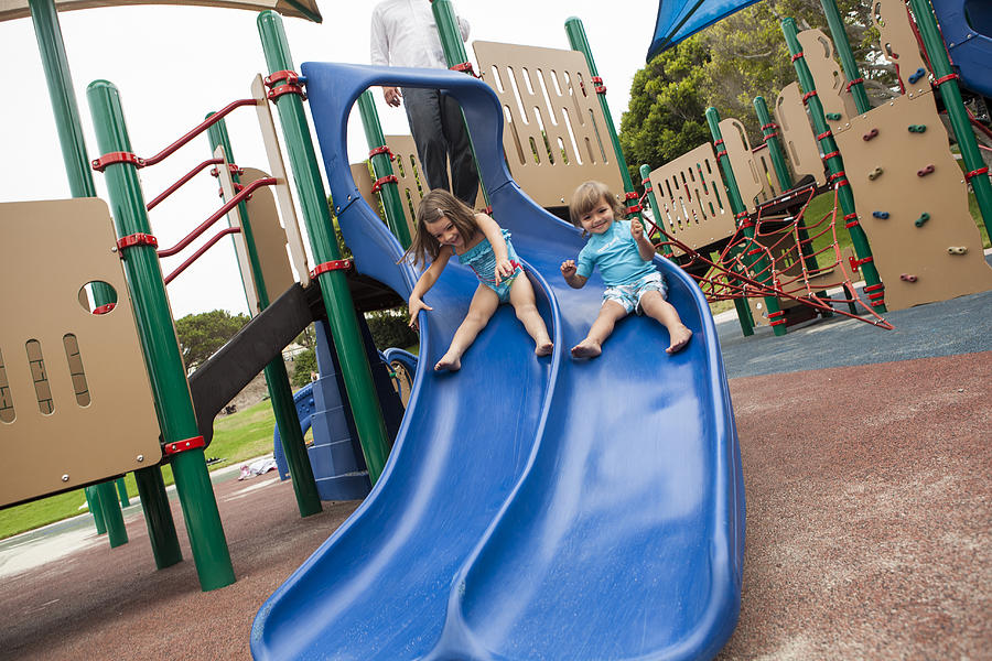 Brother and sister sliding down slide on playground Photograph by Jihan Abdalla