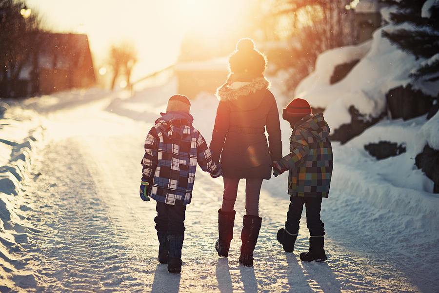 Brothers and sister walking on road on sunny winter evening. Photograph by Imgorthand