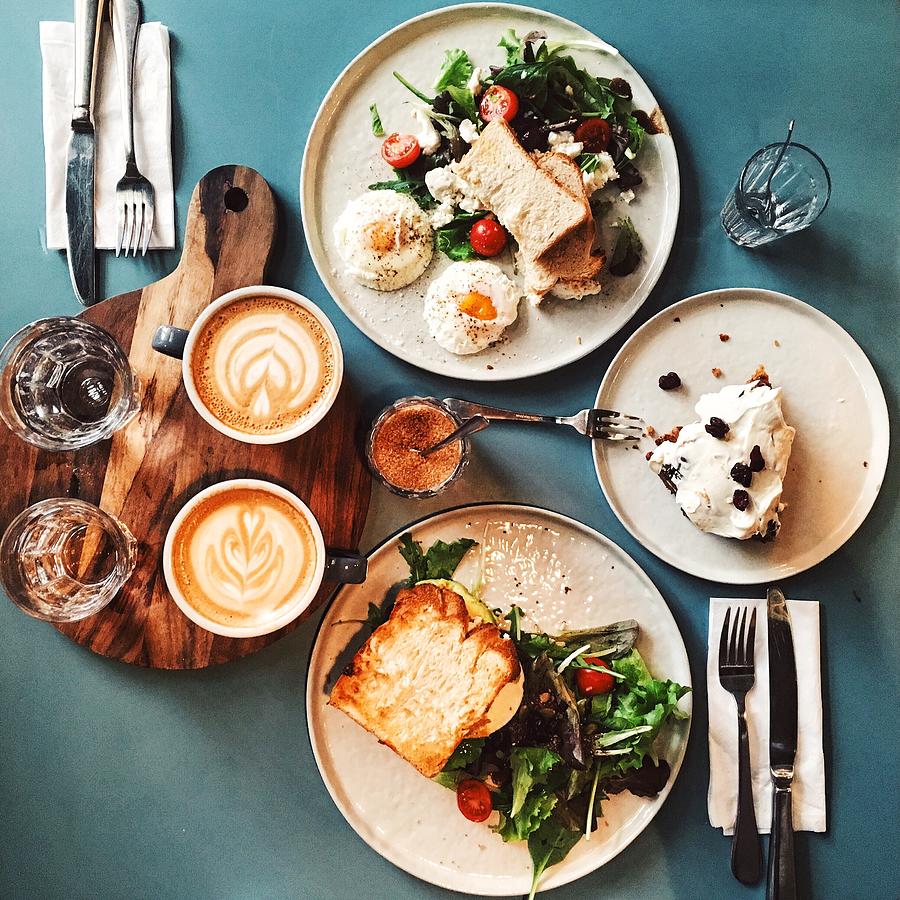 Brunch for two people with avocado toast, fried egg, salad, cappuccino and carrot cake served on the table, high angle view Photograph by Alexander Spatari