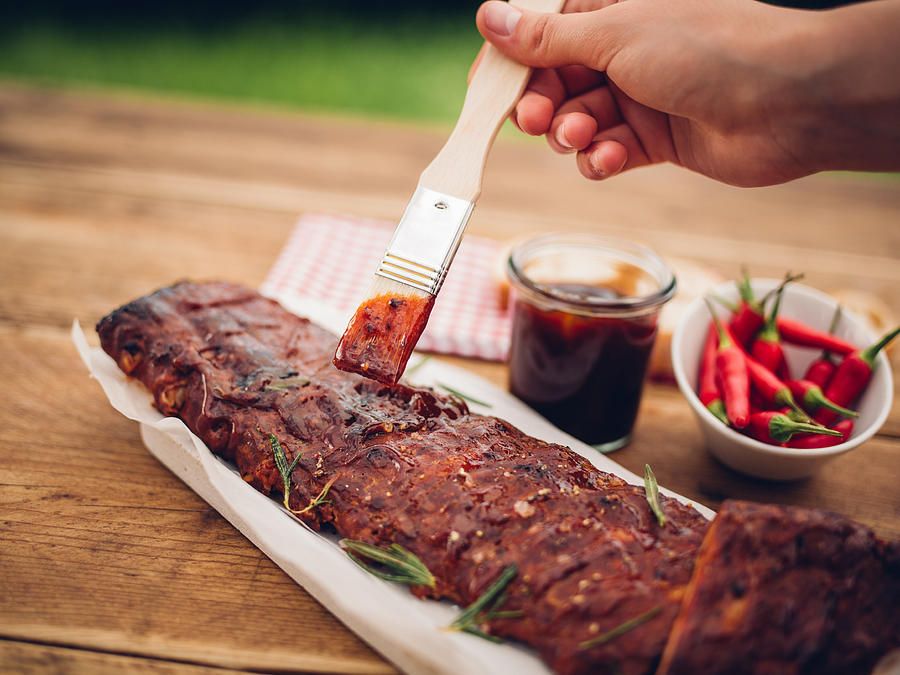 Brush painting barbecue sauce onto a rack of ribs Photograph by Wundervisuals