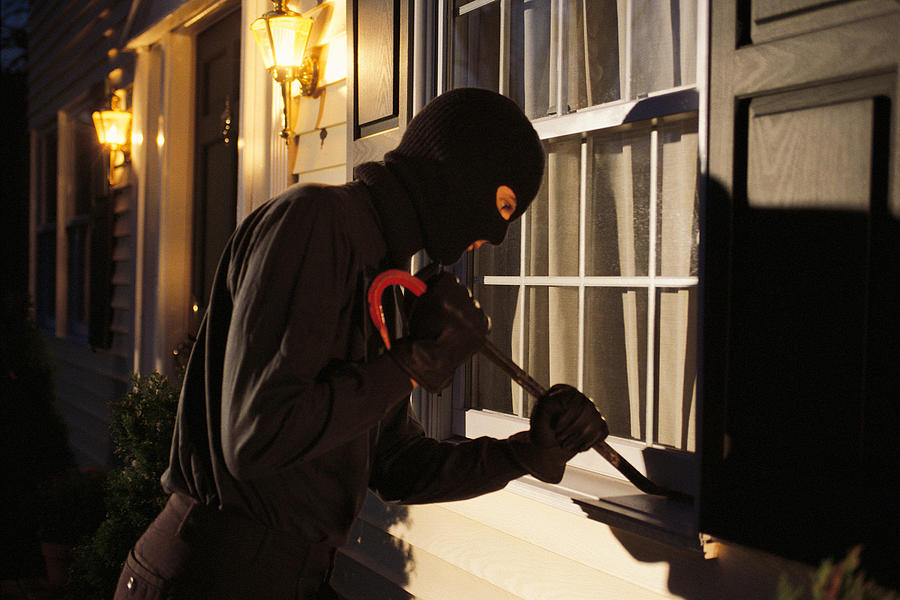 Burglar trying to pry open window on house Photograph by Comstock