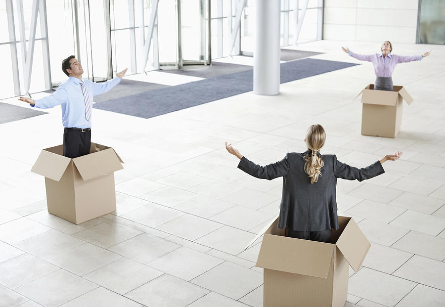 Business colleagues inside cardboard boxes with arms outstretched at new office Photograph by Clerkenwell