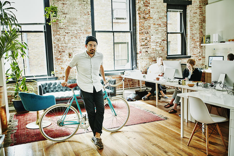 Business owner leaning against bicycle in office Photograph by Thomas Barwick