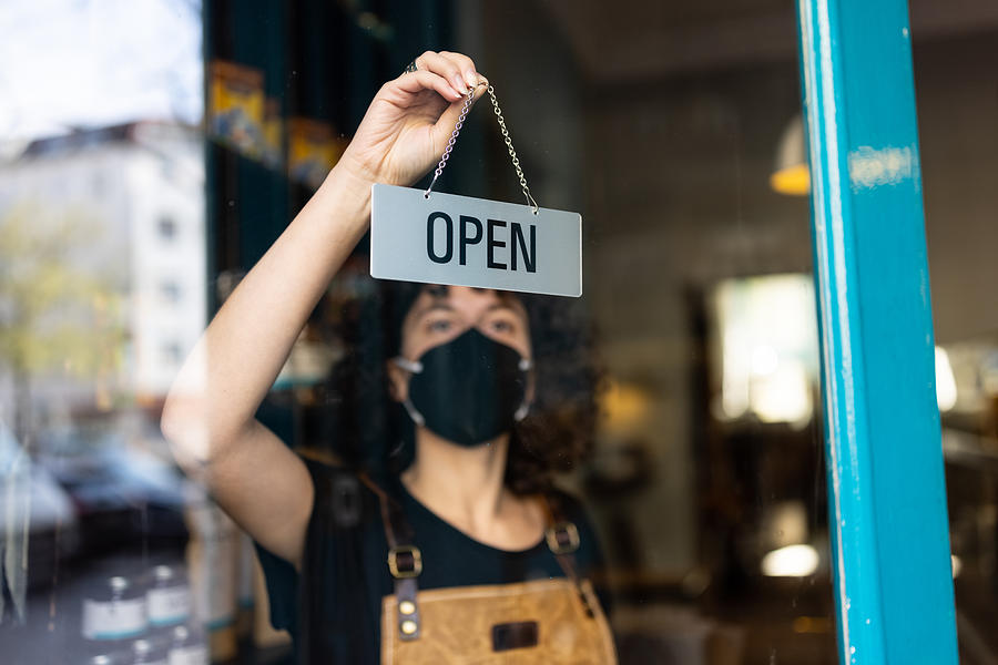 Business owner with face mask hanging an open sign at a bakery Photograph by Luis Alvarez