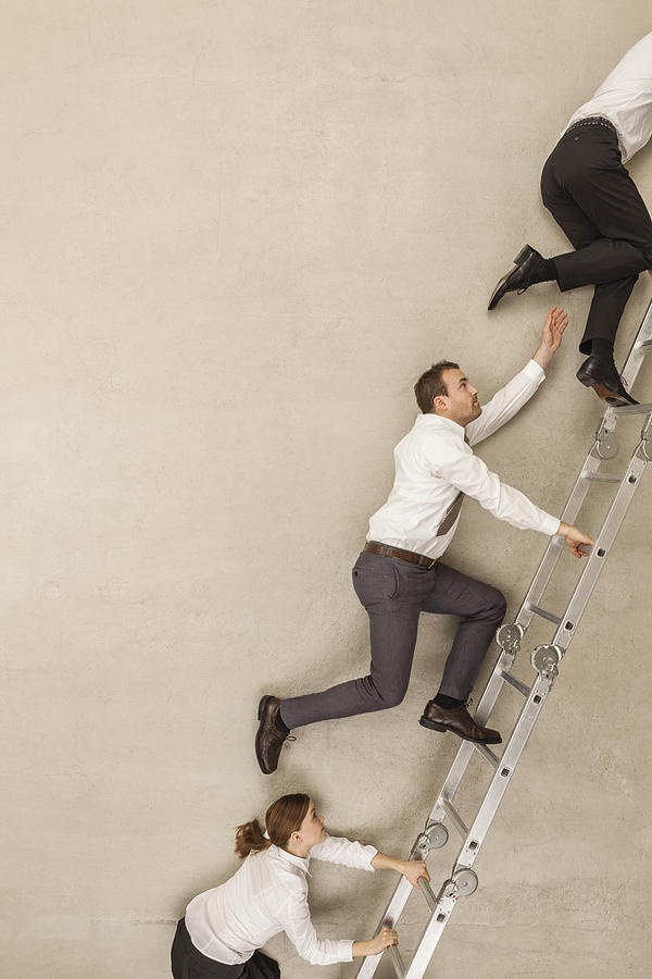 Business people climbing ladder in office Photograph by Westend61