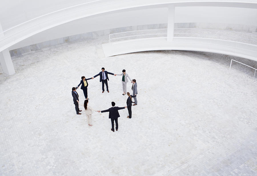 Business people holding hands in circle in courtyard Photograph by Martin Barraud