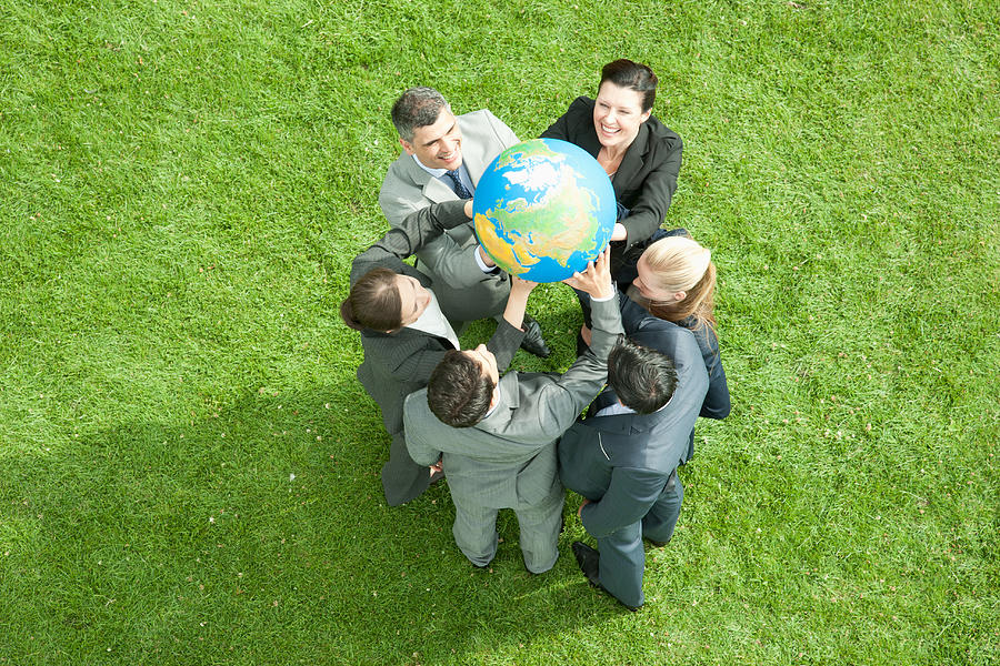 Business people lifting globe together outdoors Photograph by Martin Barraud