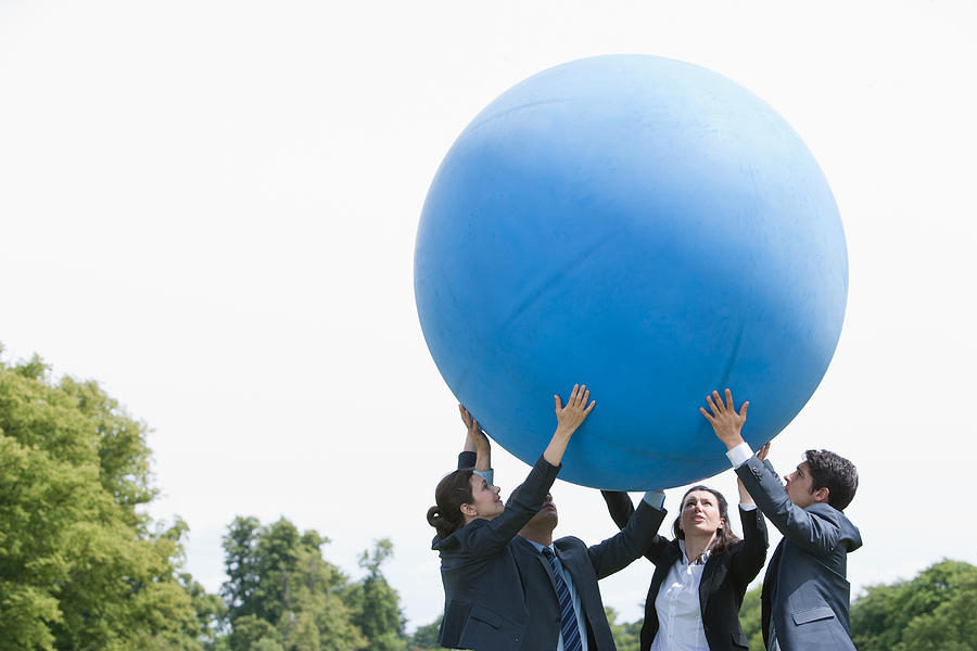 Business people lifting large ball together Photograph by Martin Barraud