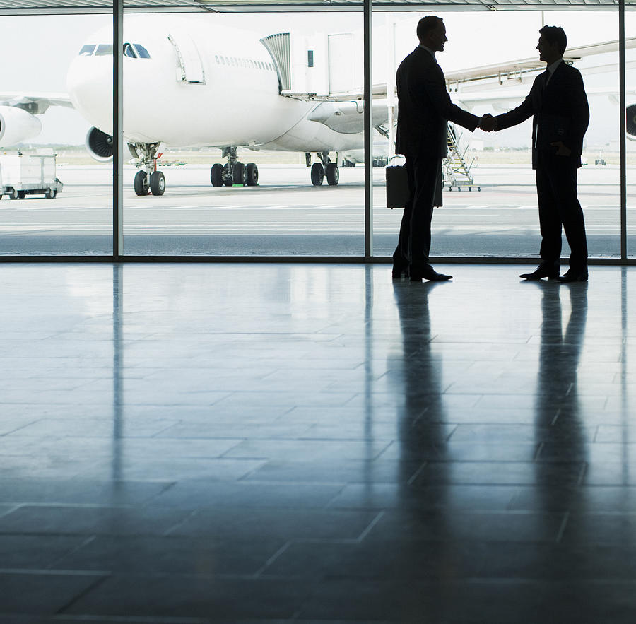 Business people shaking hands in airport Photograph by Martin Barraud