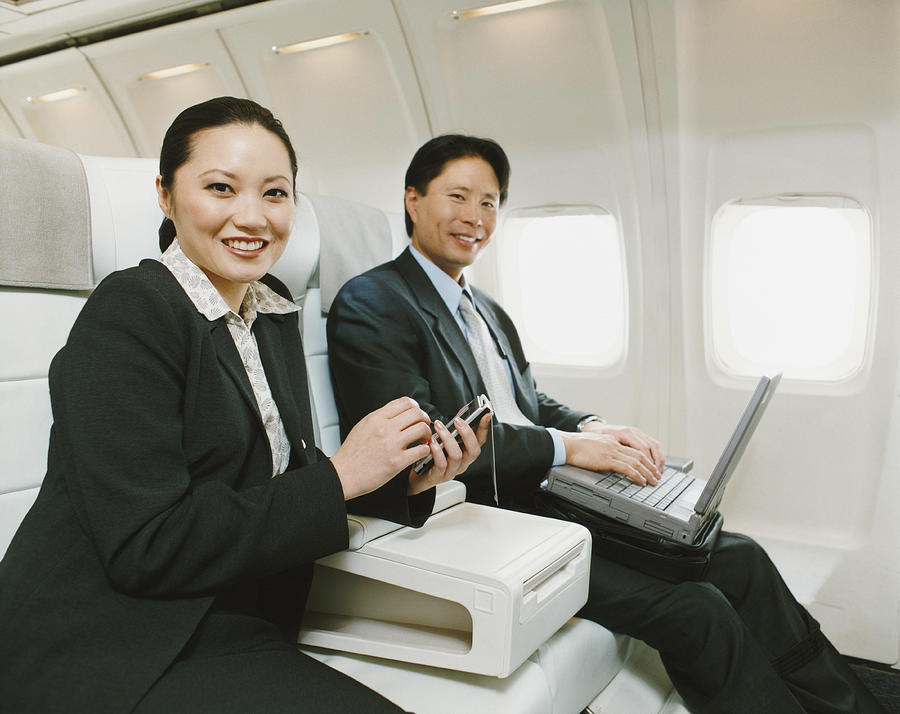 Business People Sitting in an Aircraft With Palm Pilot and Laptop Photograph by Digital Vision.