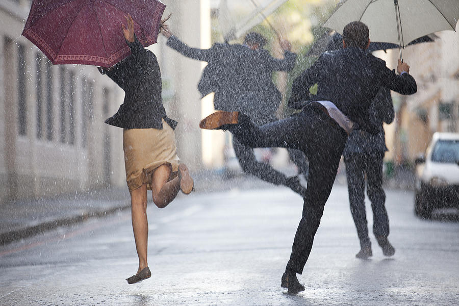 Business people with umbrellas dancing in rain Photograph by Caia Image