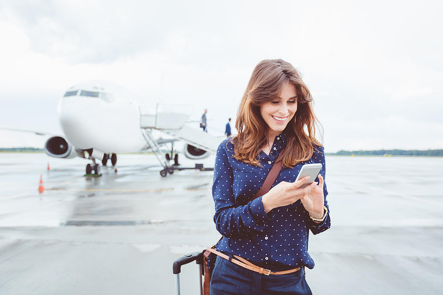 Business woman using a smart phone in front of airplane Photograph by Izusek