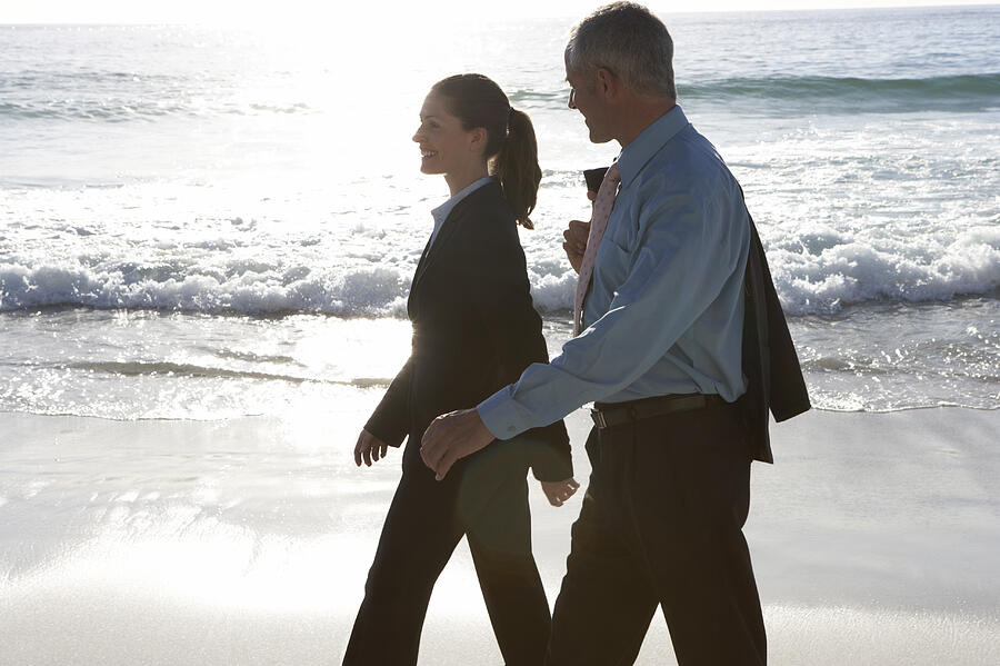 Businessman and a Businesswoman Walking at the Waters Edge on a Beach Photograph by John Cumming