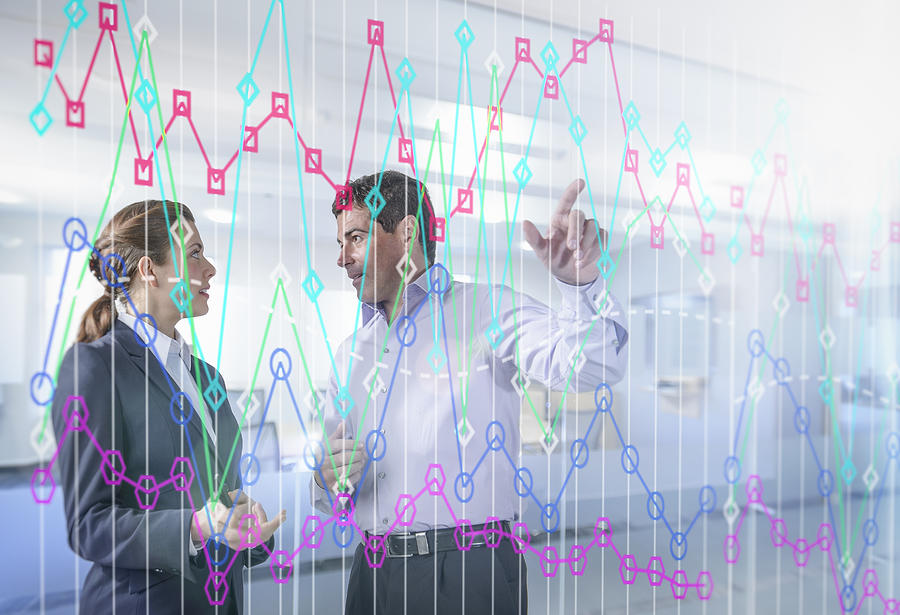 Businessman and businesswoman discussing graph on interactive display Photograph by Monty Rakusen