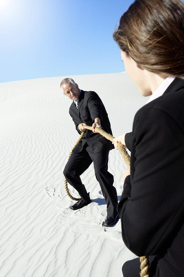 Businessman and Businesswoman Playing Tug of War in a Desert Photograph by John Cumming