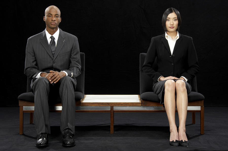 Businessman and businesswoman sitting at opposite ends of bench Photograph by James Woodson
