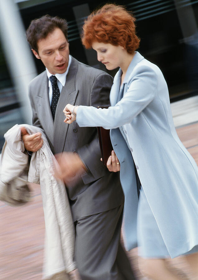 Businessman and businesswoman walking side by side outside, businessman looking at watch Photograph by Eric Audras