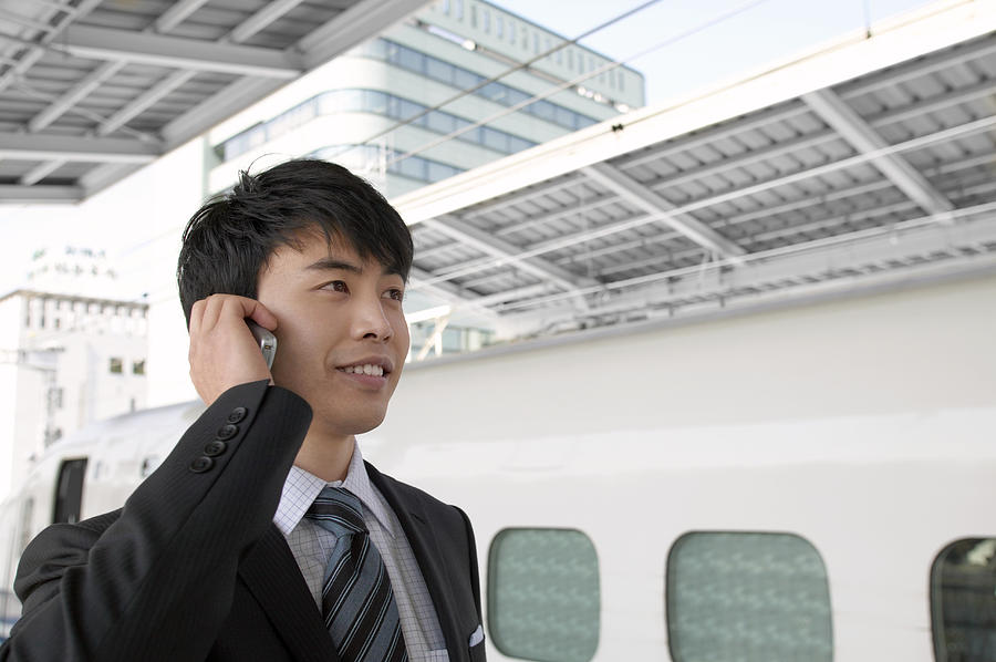 Businessman at a Train Station Using a Mobile Phone Photograph by Digital Vision.