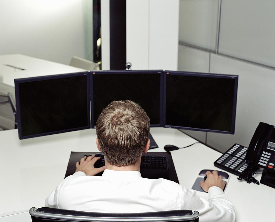 Businessman at desk using computer with multiple screens, rear view Photograph by Digital Vision
