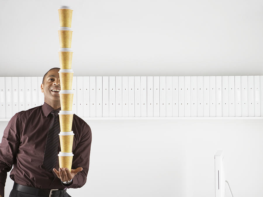Businessman balancing large stack of paper coffee cups Photograph by Anthony Lee