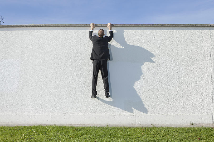 Businessman climbing over wall Photograph by Johnny Valley