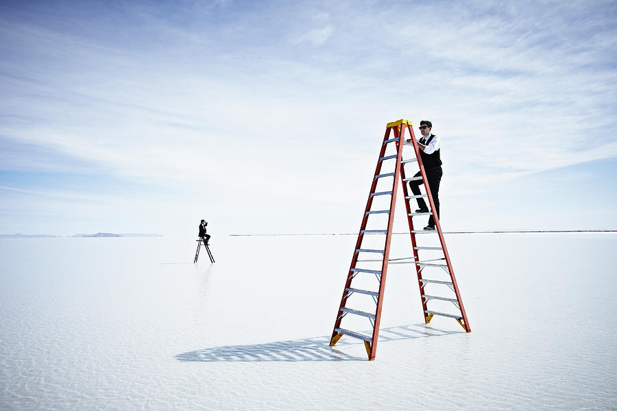 Businessman climbing tall ladder in lake Photograph by Thomas Barwick