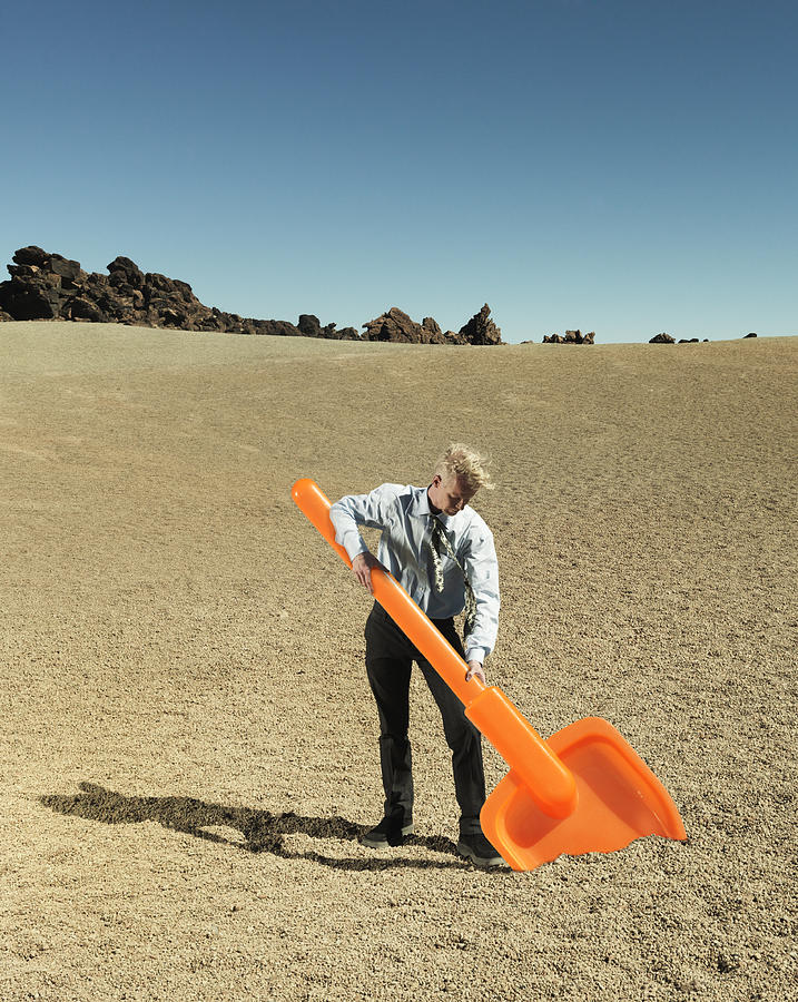 Businessman digging with oversized plastic spade Photograph by Henrik Sorensen