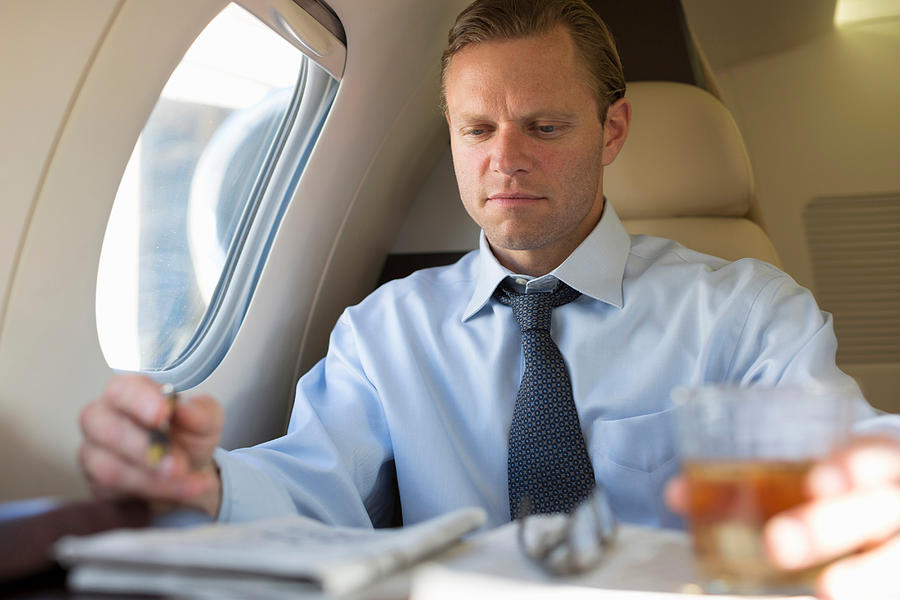 Businessman doing crossword on airplane Photograph by Image Source/InStock