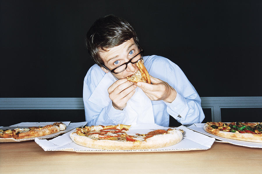 Businessman eating pizza from boxes on table, portrait Photograph by Pando Hall