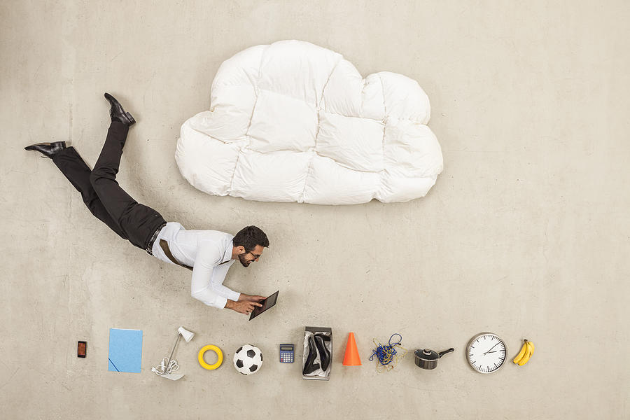 Businessman flying between cloud shape pillow and variety of items Photograph by Westend61