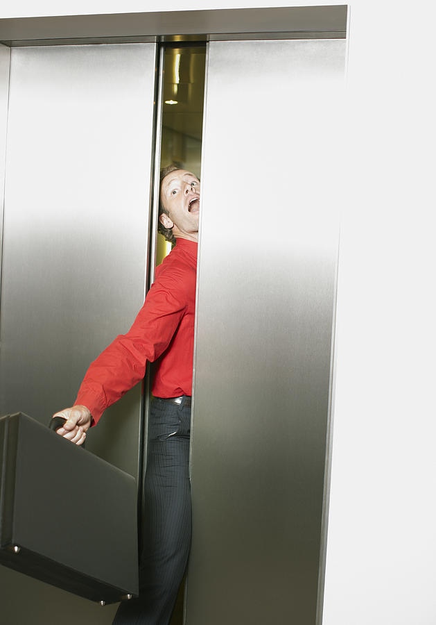 Businessman getting stuck in elevators doors Photograph by Paul Bradbury